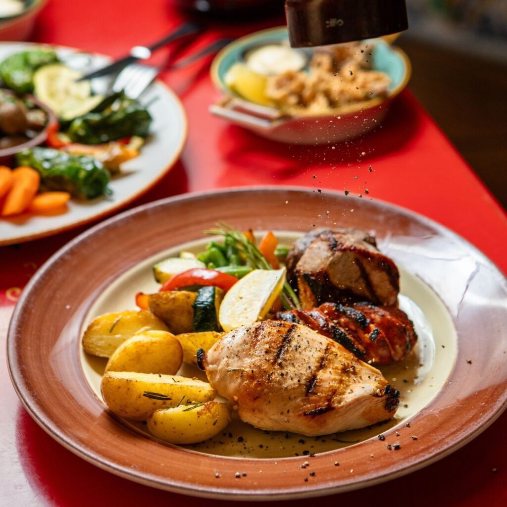 Nahaufnahme einer gegrillten Hähnchenbrust, serviert mit Kartoffeln und Zitrone auf einem Keramikteller.