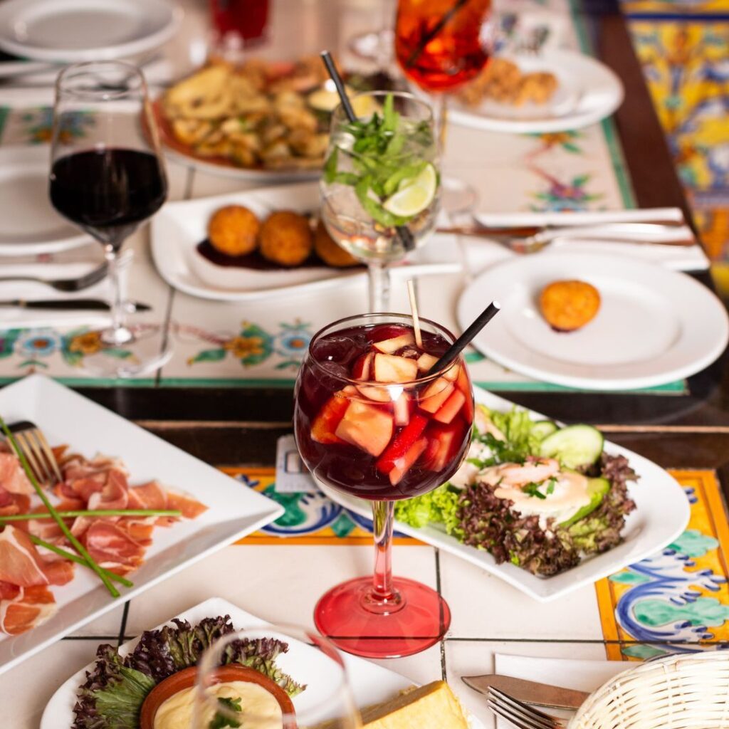 Ein Glas Sangria mit verschiedenen traditionellen spanischen Tapas, serviert auf einem dekorativen Mosaiktisch im Vivolo Olé in Berlin.