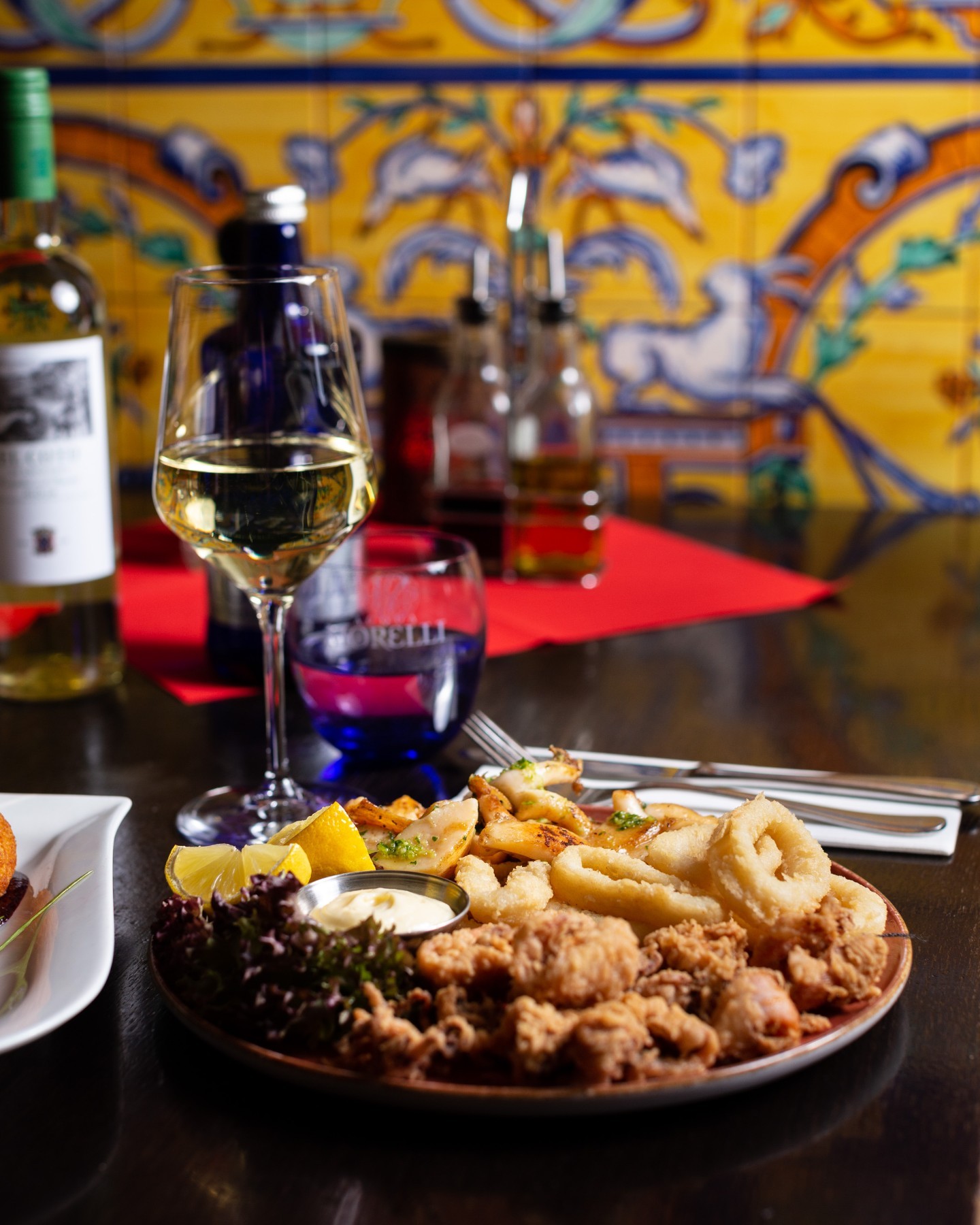Plate of fried calamari and seafood with lemon wedges and a glass of white wine.