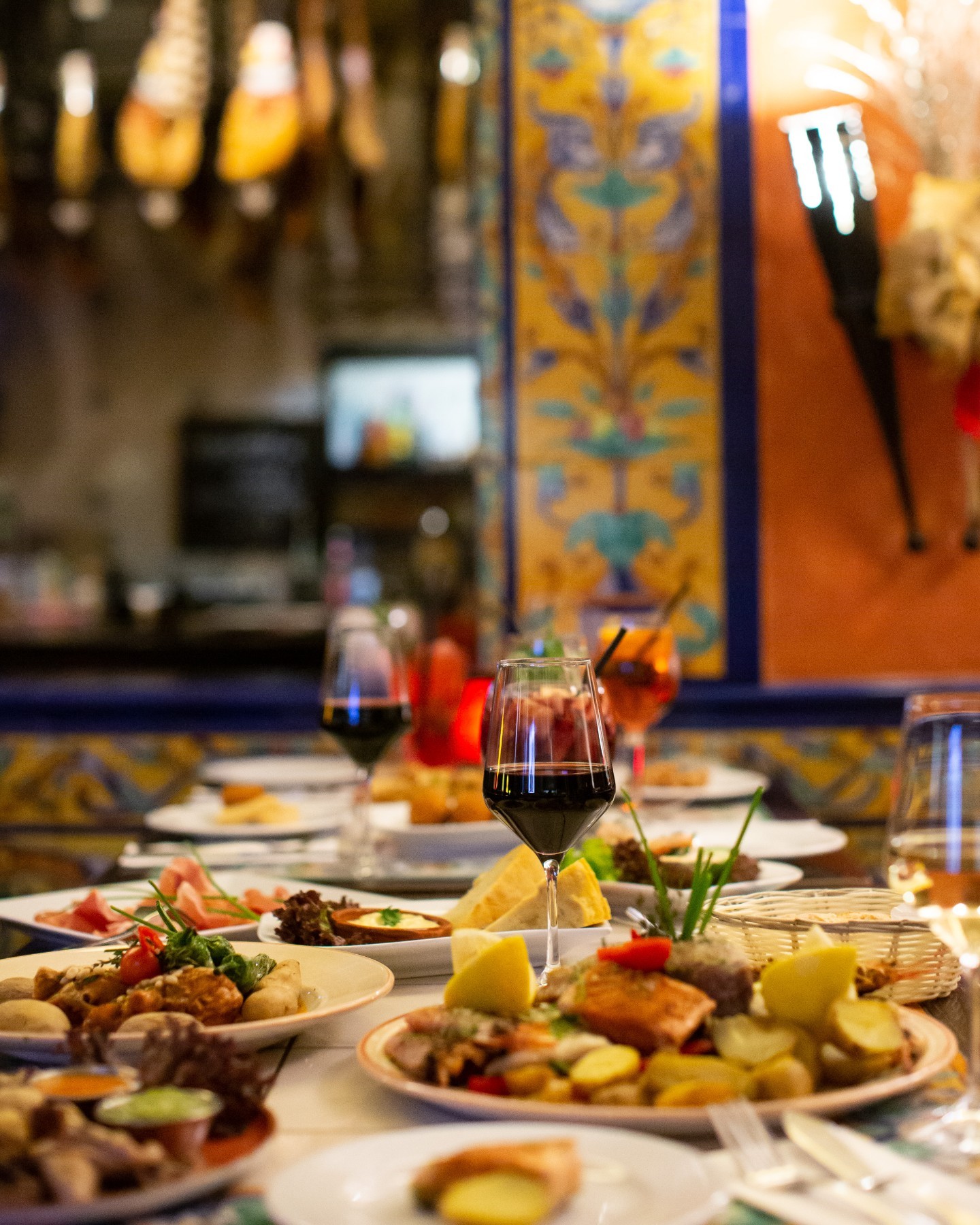 Spanish tapas and wine set on a long dinner table with vibrant decor in the background.
