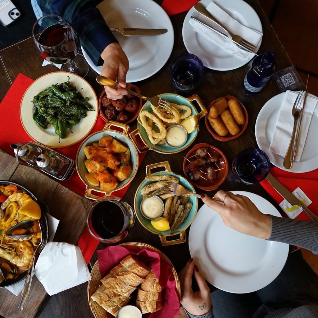 Draufsicht auf einen Tisch voller spanischer Tapas-Gerichte, Hände reichen Speisen.