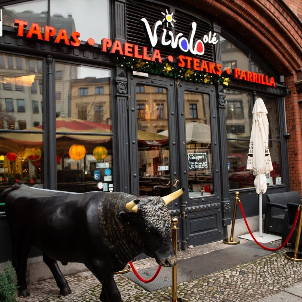 Vordereingang des spanischen Restaurants Vivolo Olé in Berlin mit einer dekorativen schwarzen Stierstatue.