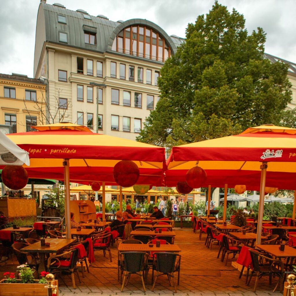 Außenterrasse des spanischen Restaurants Vivolo Olé in Berlin mit roten und gelben Sonnenschirmen und Holztischen.